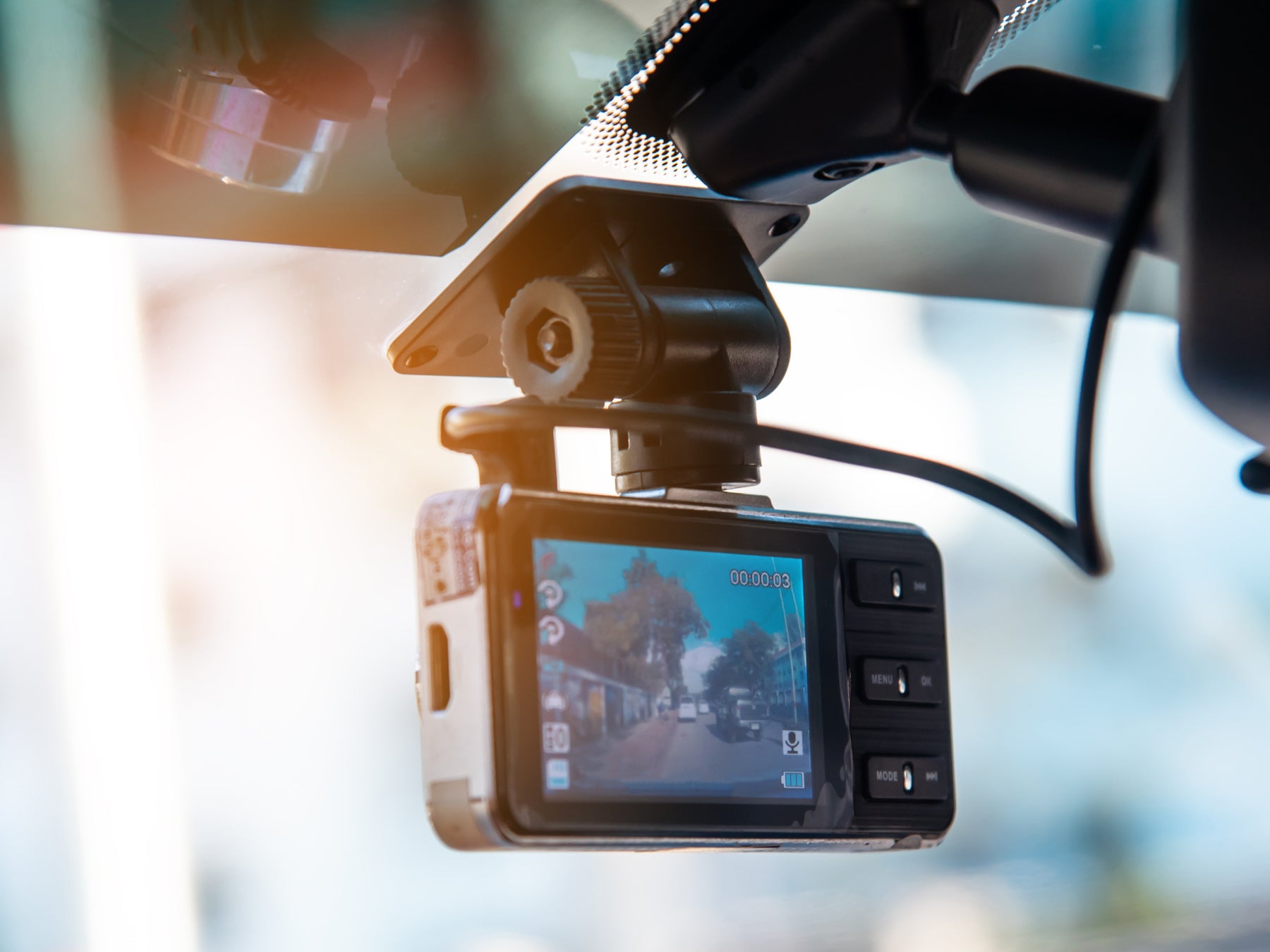 Car dashboard camera mounted on a car's windshield with a blurred street view in the display.